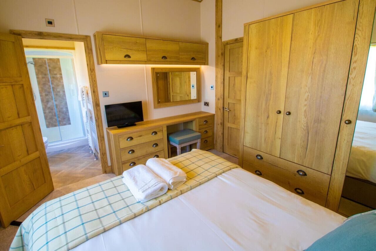 Een slaapkamer met een bed, een bureau met een televisie, een spiegel en houten kasten.