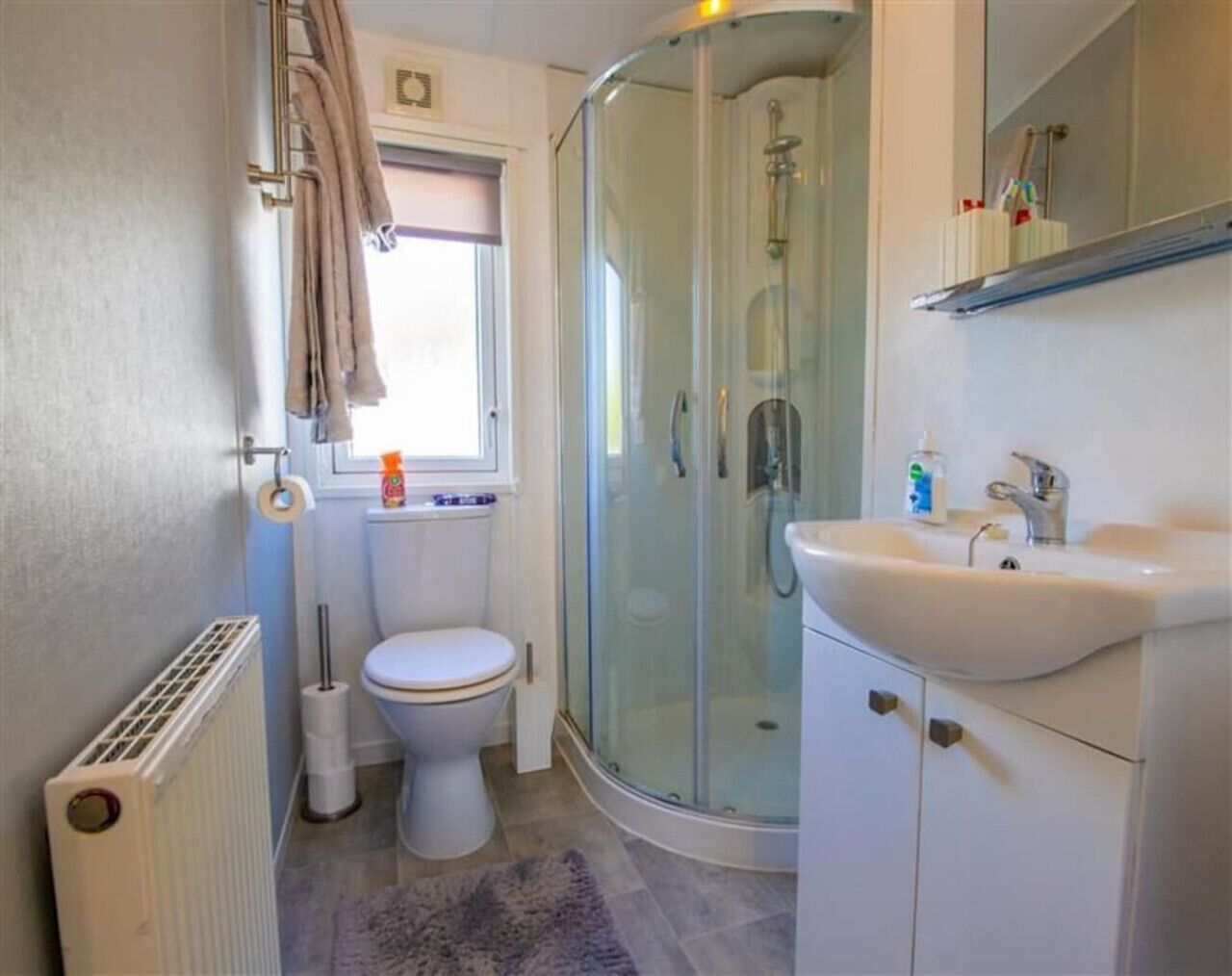 Un baño con inodoro, cabina de ducha de vidrio, lavamanos y ventana.