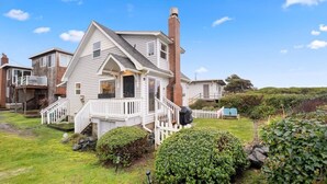 A two-story house with a white exterior, a brick chimney, and a white picket fence. - #StayInMyDistrict SurfsideHaven (Rockaway Beach)