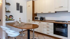 A modern kitchen with white cabinets, a microwave, a gas stove, and a dining area with a wooden table and white bar stools.