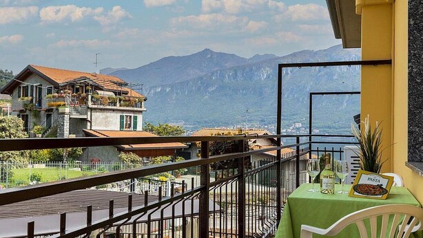 A balcony with a table set for dining, overlooking a mountainous landscape.