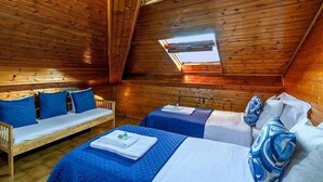 A cozy cabin room with wooden walls and a sloped ceiling, featuring two beds with blue bedding and a wooden bench.