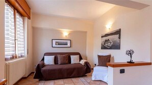 A cozy room with a brown sofa, a white chair, a small table with a decorative item, and a framed picture on the wall.