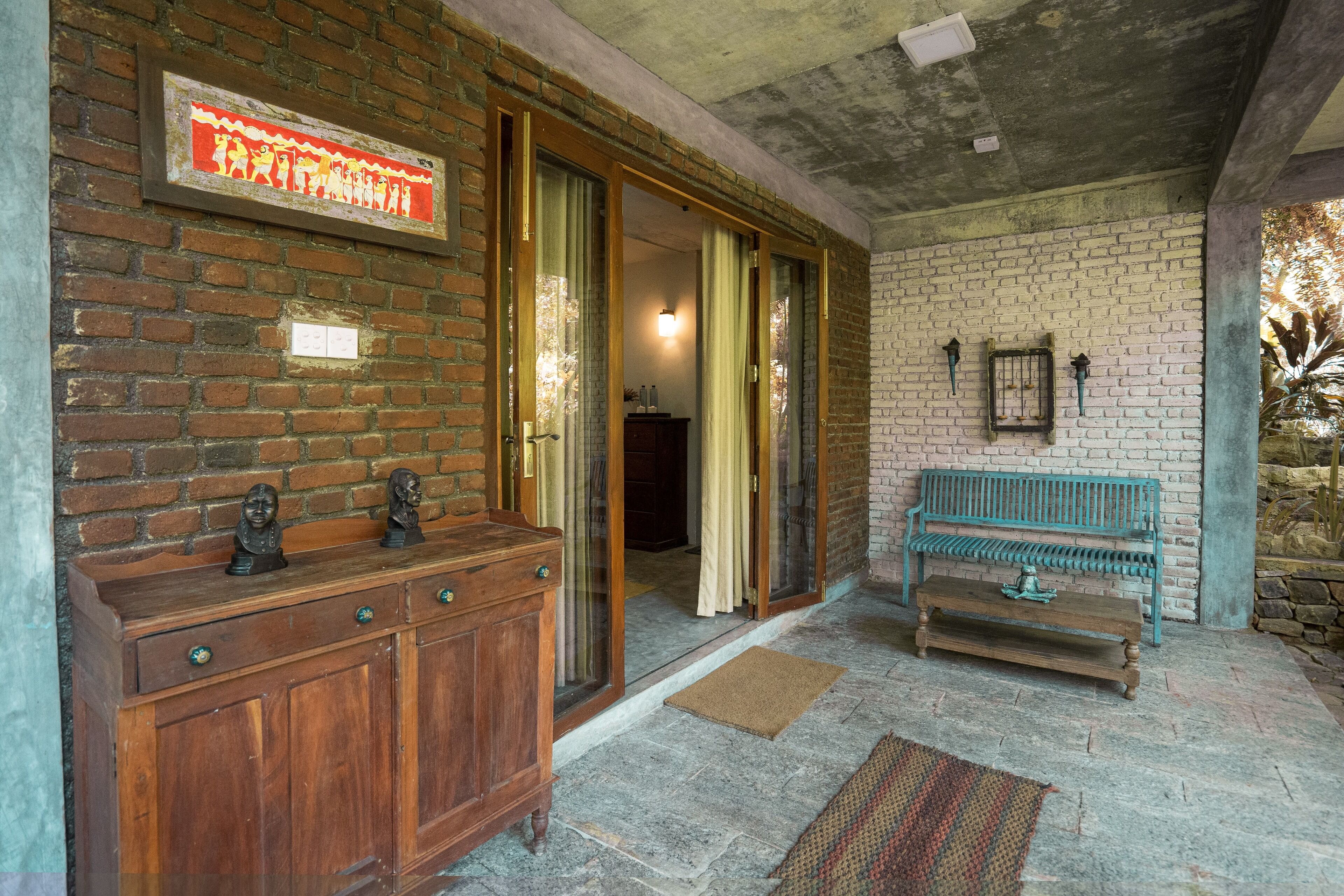 A brick wall with a framed picture, a wooden bench, and a door leading to another room.