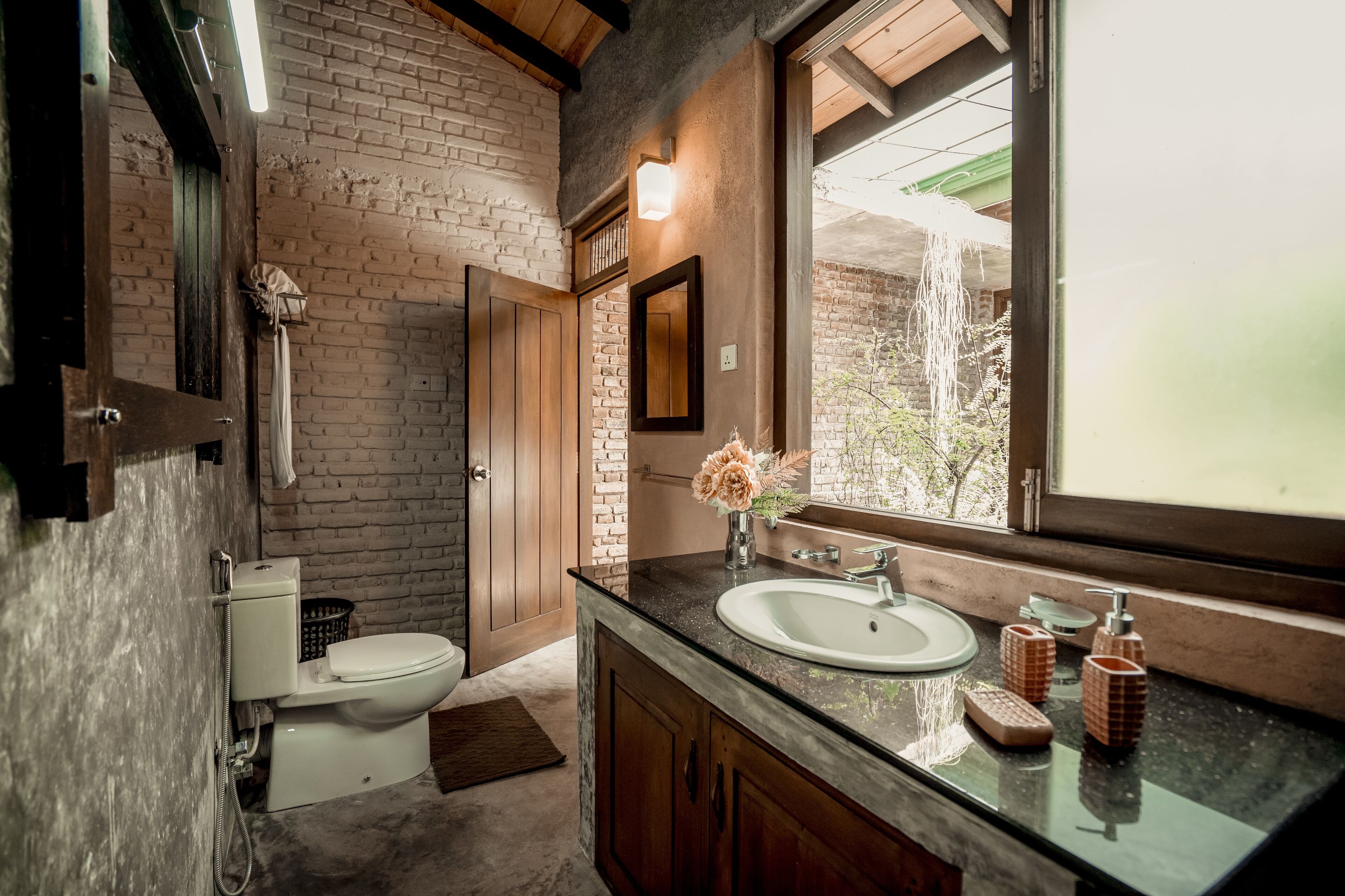Une salle de bain avec un mur en briques, des meubles en bois, une grande fenêtre et des toilettes.