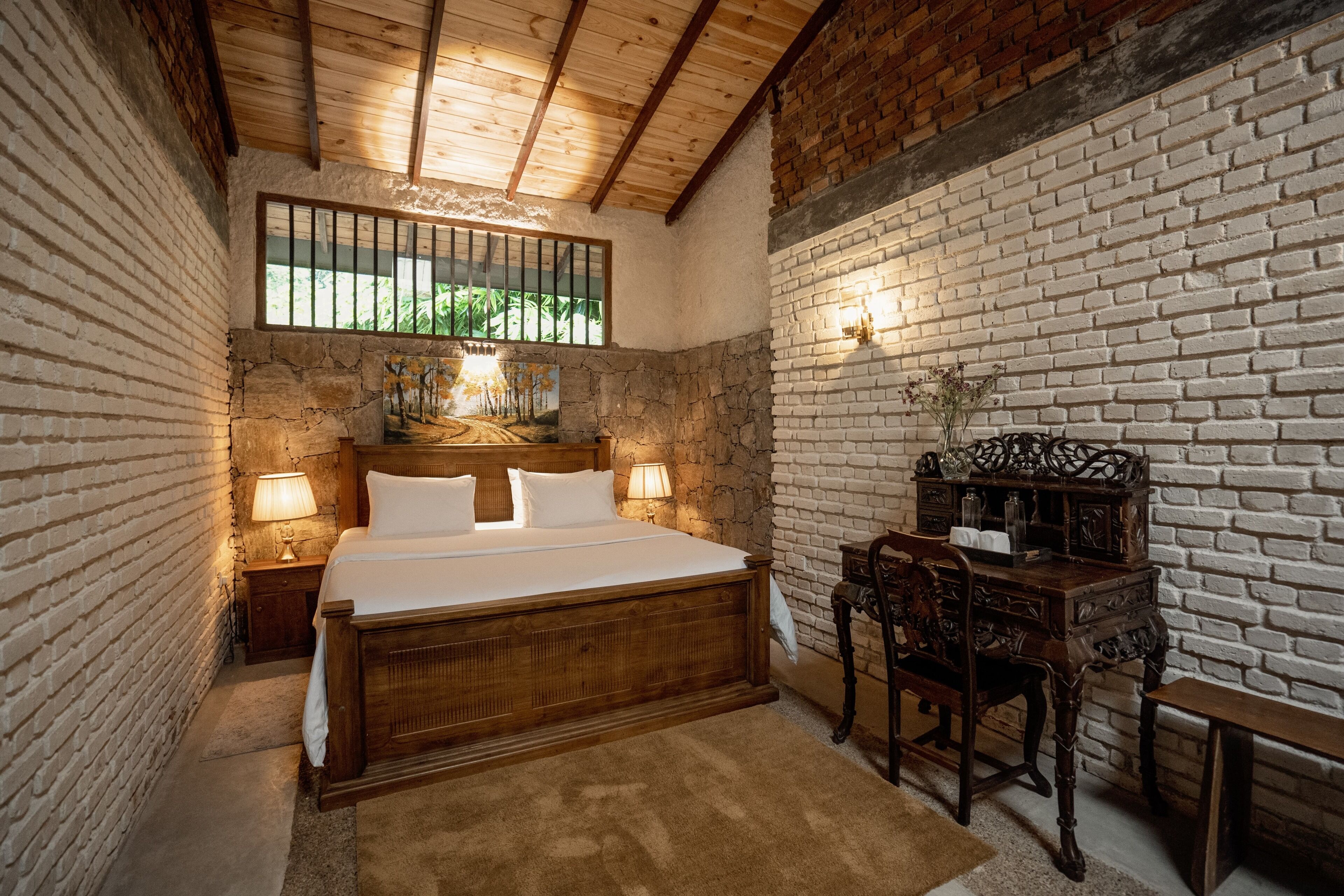 Een slaapkamer met een houten bed, een nachtkastje, een bureau met stoel en een bakstenen muur.
