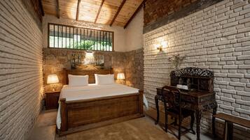 Een slaapkamer met een houten bed, een nachtkastje, een bureau met stoel en een bakstenen muur.