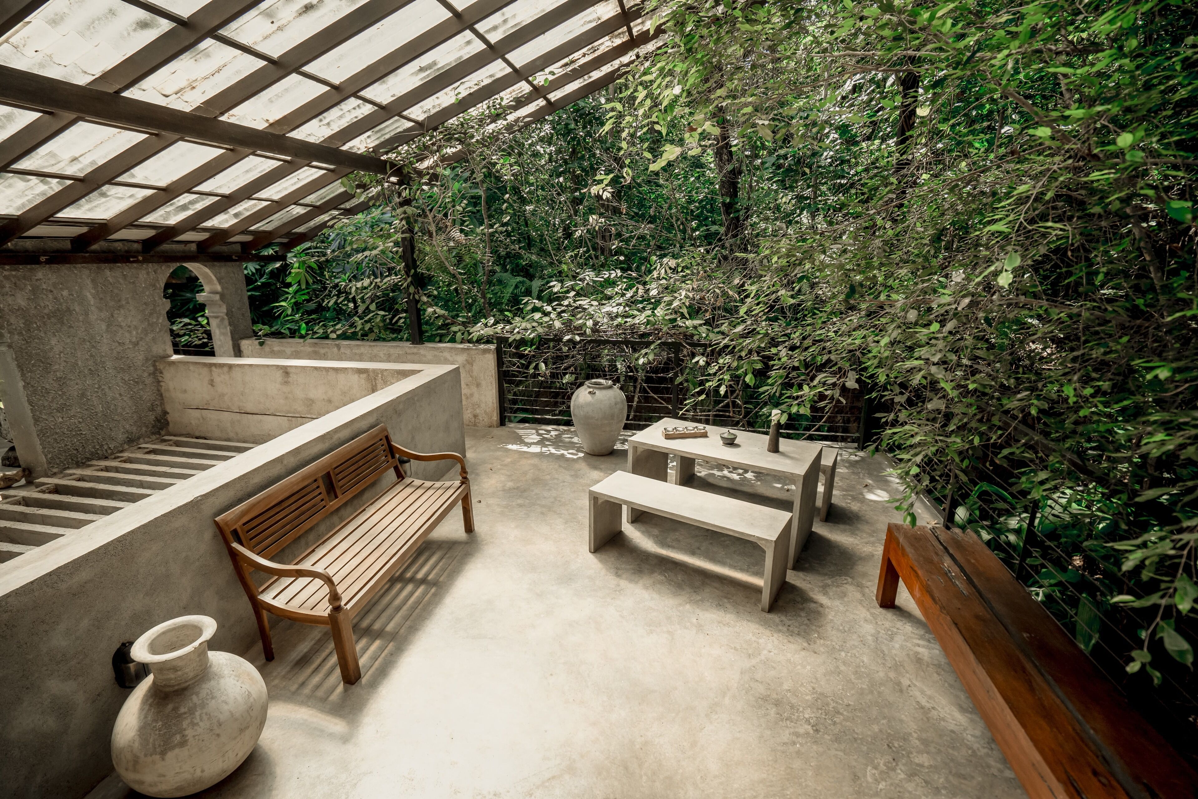 An outdoor patio with a wooden bench, a concrete table, and a large vase.