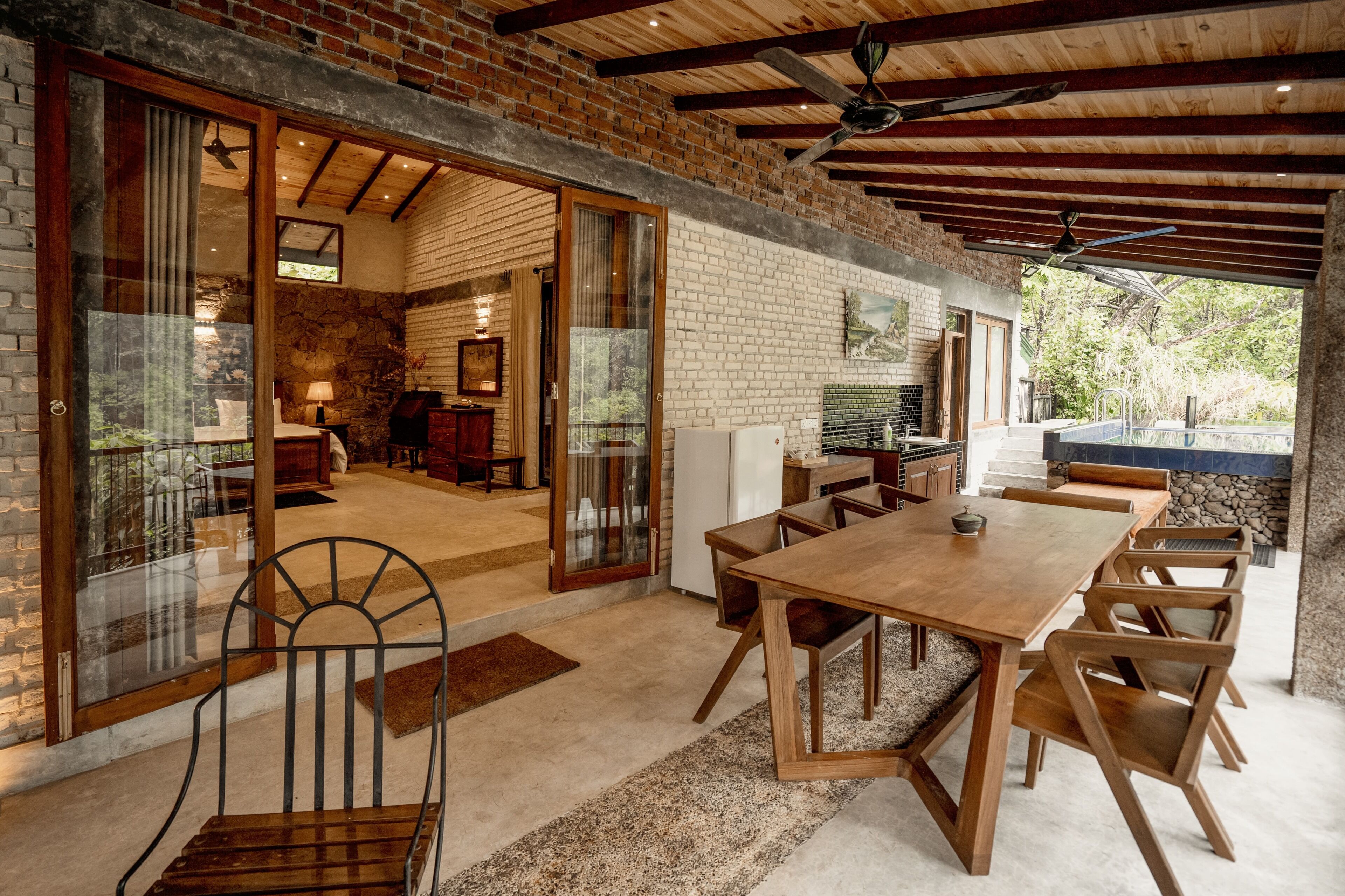 A spacious dining area with a large wooden table and chairs, a stone wall, and a view of the outdoors.