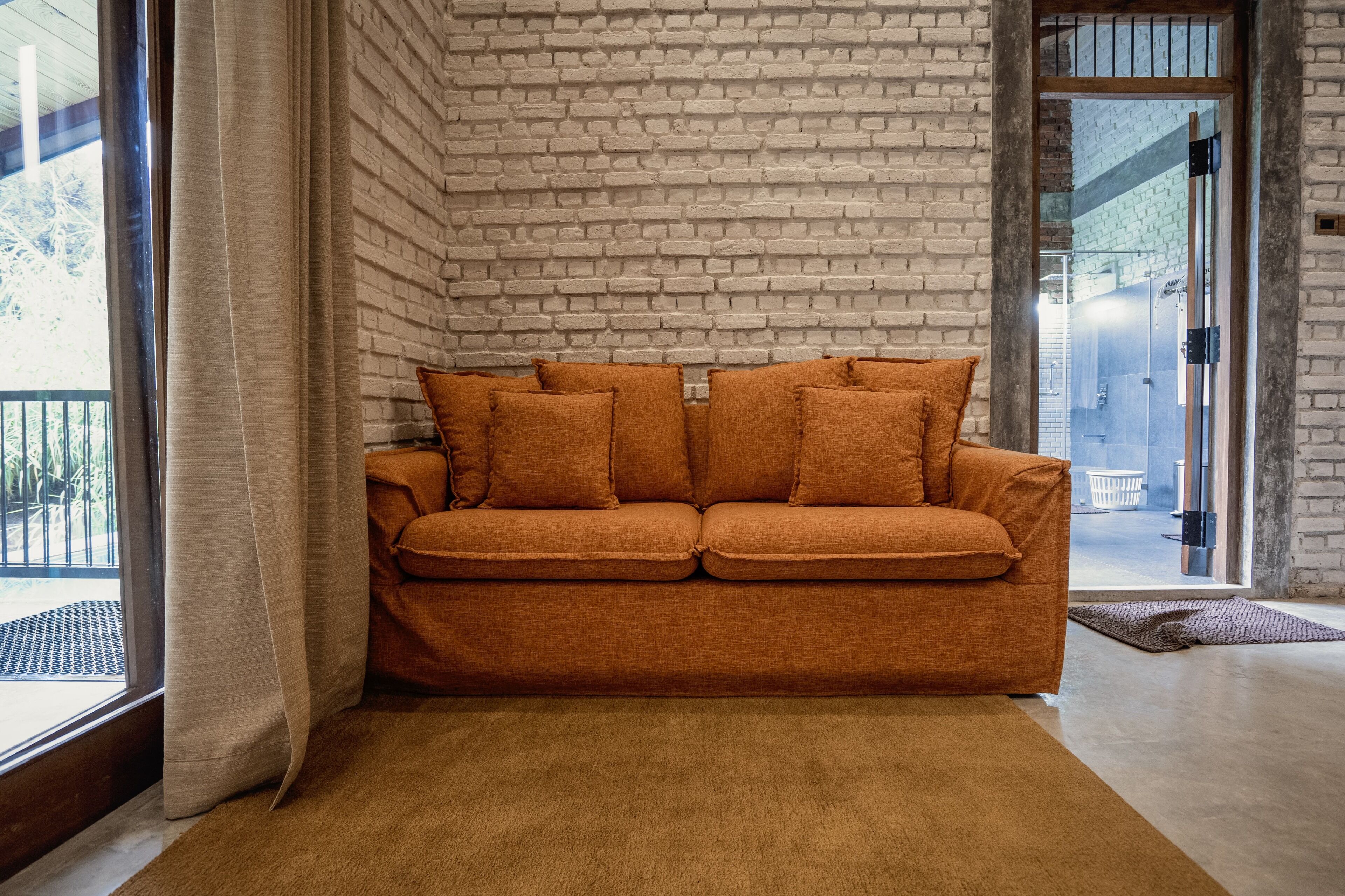 A room with a brick wall, a brown sofa, and a large window.