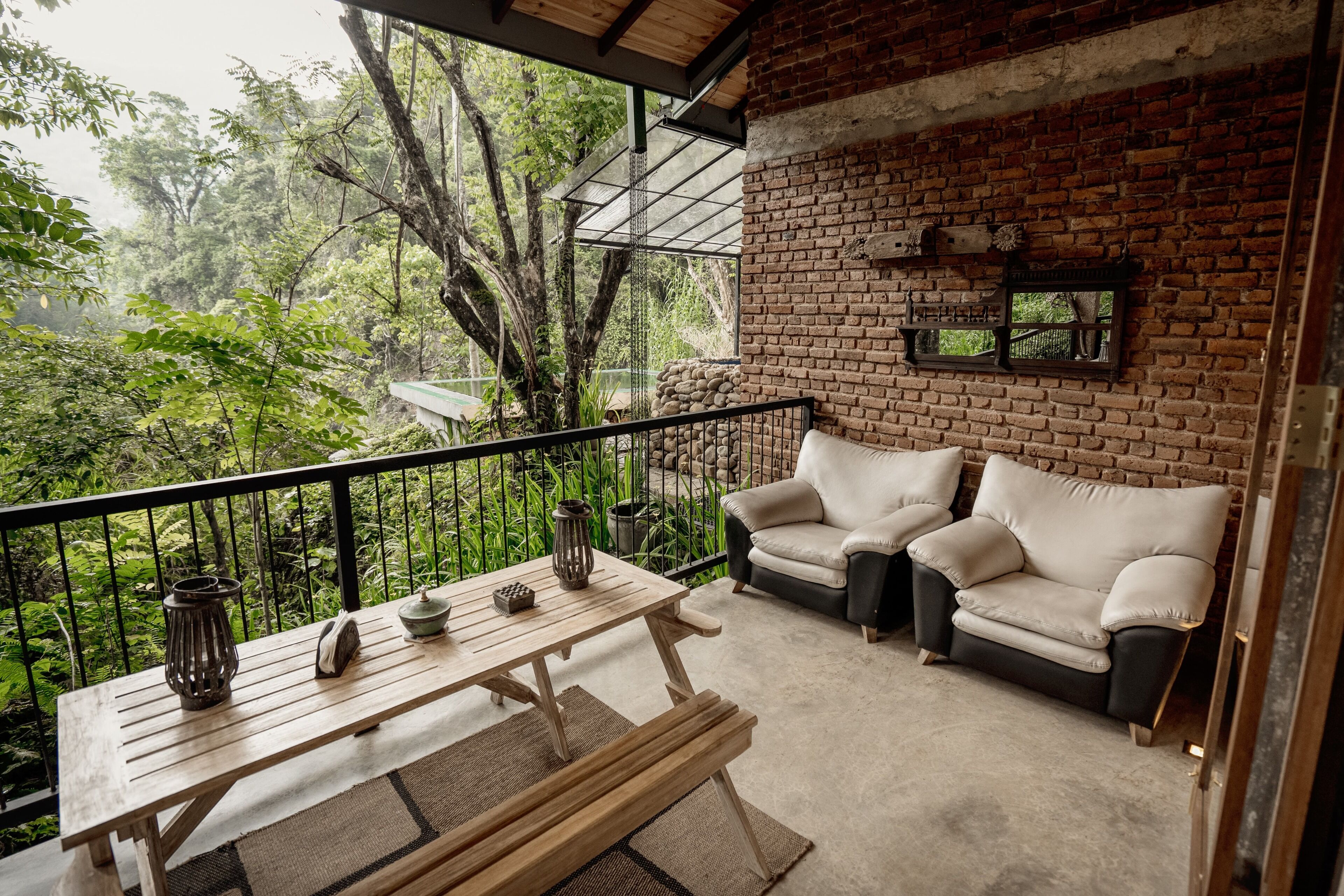 A balcony with a wooden table, two cushioned chairs, and a view of lush greenery.
