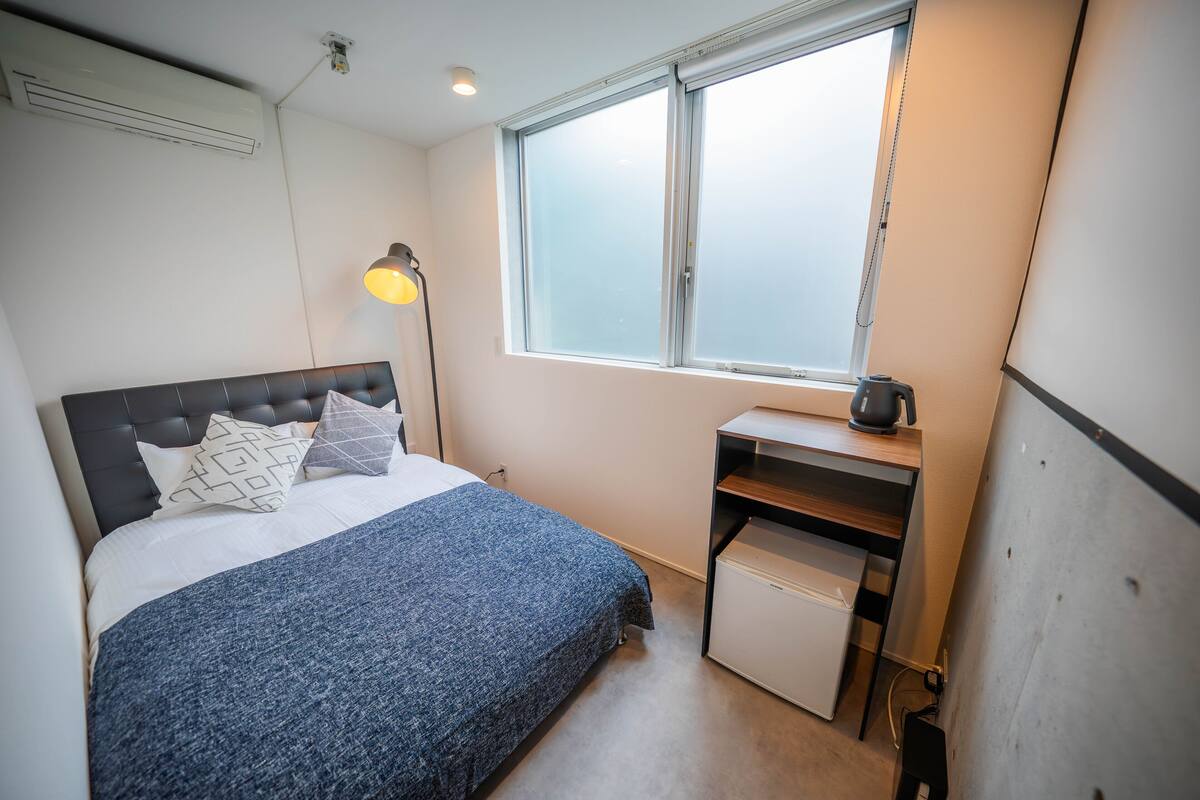A bedroom with a bed, a desk, a lamp, and a window.