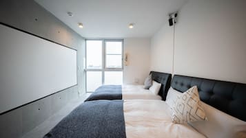 A modern hotel room with two beds, a large window, and a flat-screen TV mounted on the wall.