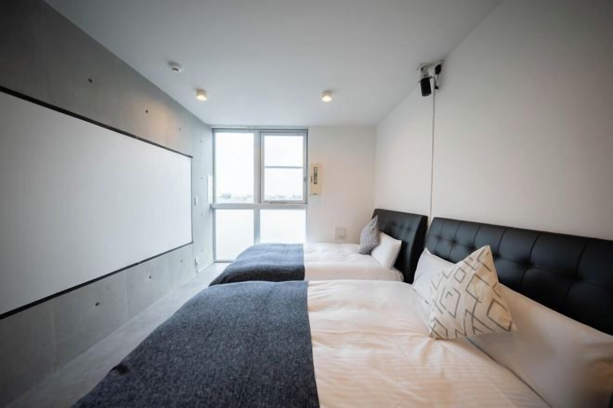 Une chambre avec un grand lit, un plus petit lit et un banc. Une fenêtre laisse entrer la lumière naturelle.