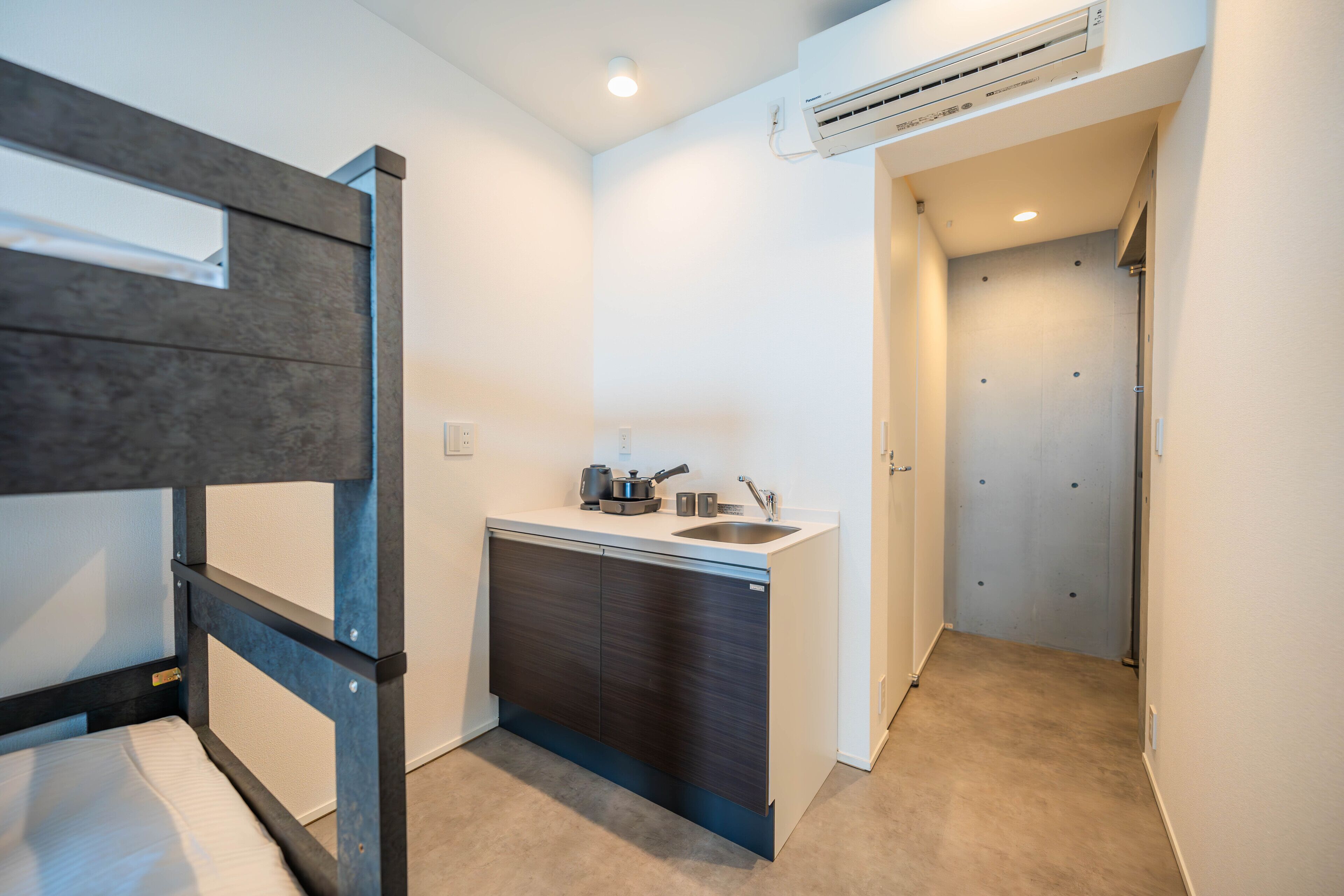 Una habitación compacta con una cama litera, una kitchenette con un lavamanos y una puerta que da a otra habitación.