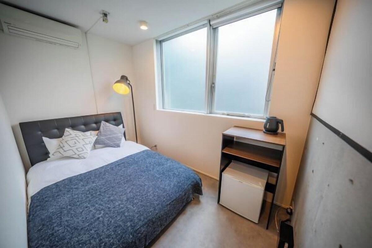 A bedroom with a bed, a desk, a lamp, and a window.