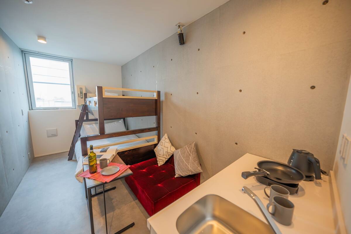 A compact room with a bunk bed, a kitchenette with a sink, and a window providing natural light.