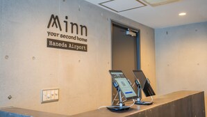 Un comptoir d'accueil avec une pancarte indiquant « Minn, votre deuxième maison à l’aéroport de Haneda », ainsi que deux bornes numériques.