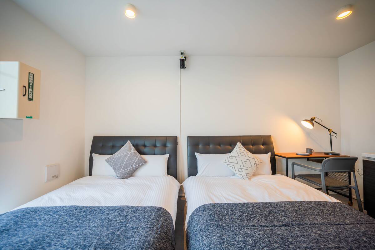 A twin room with two beds, a desk, a chair, and a lamp.