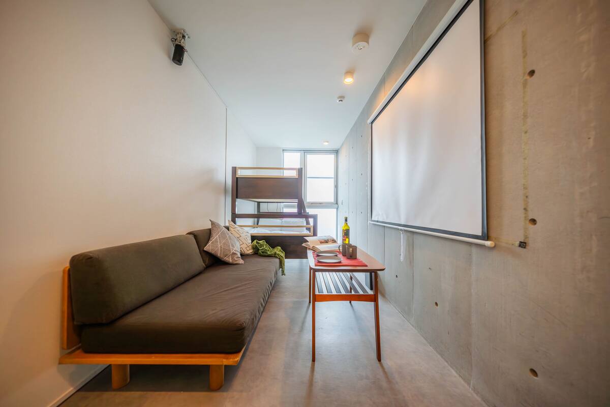 A modern room with a sofa, a small table, and a projector screen on the wall.