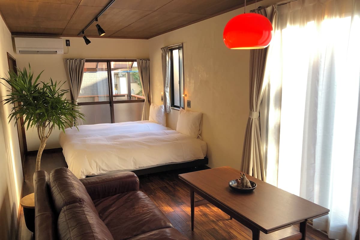 Quarto de hotel com cama, sofá, mesa, planta em vaso e janela com cortinas.