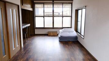 A room with a large window, a bed, a small wooden table, and a chair.