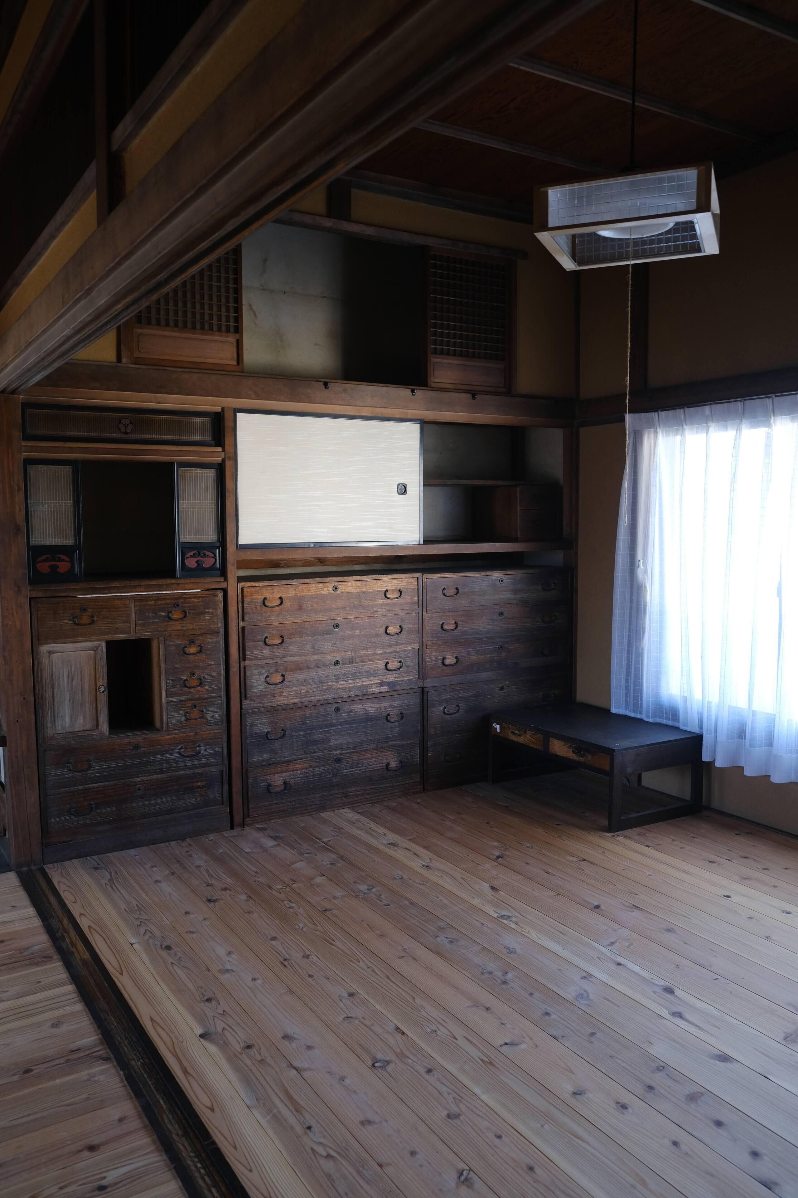 Una habitación tradicional japonesa con suelo de madera, armarios empotrados, una pequeña mesa y un ventilador de techo.