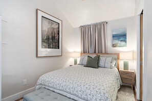 Una camera da letto con un letto, due comodini, una testiera, una finestra con tende e due lampade a parete.