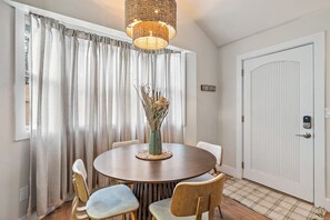 Un comedor con una mesa redonda, sillas, un jarrón con plantas secas y una puerta con mirilla.