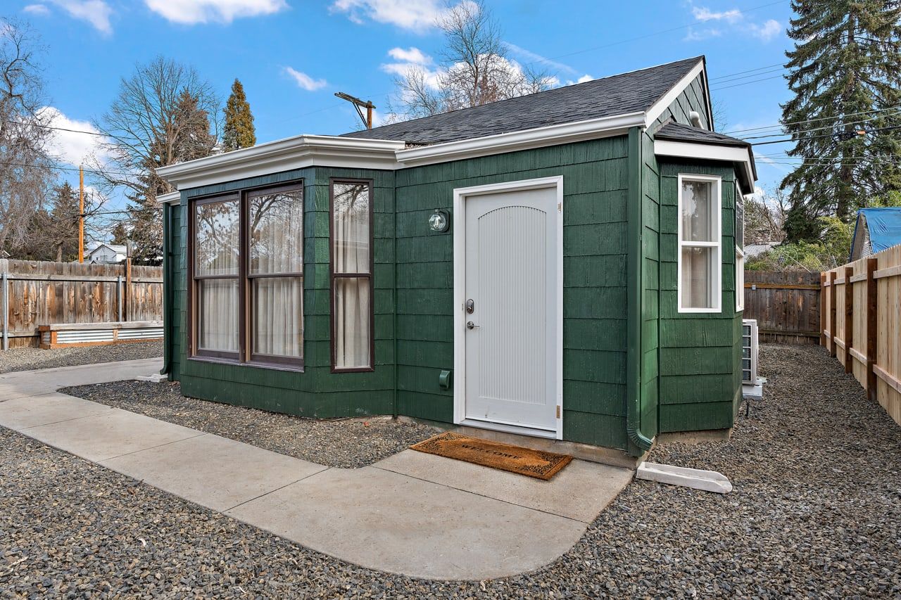 A small, single-story building with a white door and windows, surrounded by gravel and a wooden fence.