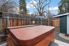 Una vasca idromassaggio in un giardino privato, con un recinto in legno, un capanno e un albero.