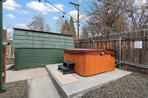Un jacuzzi en un patio trasero con valla de madera, un cobertizo verde y una puerta metálica.