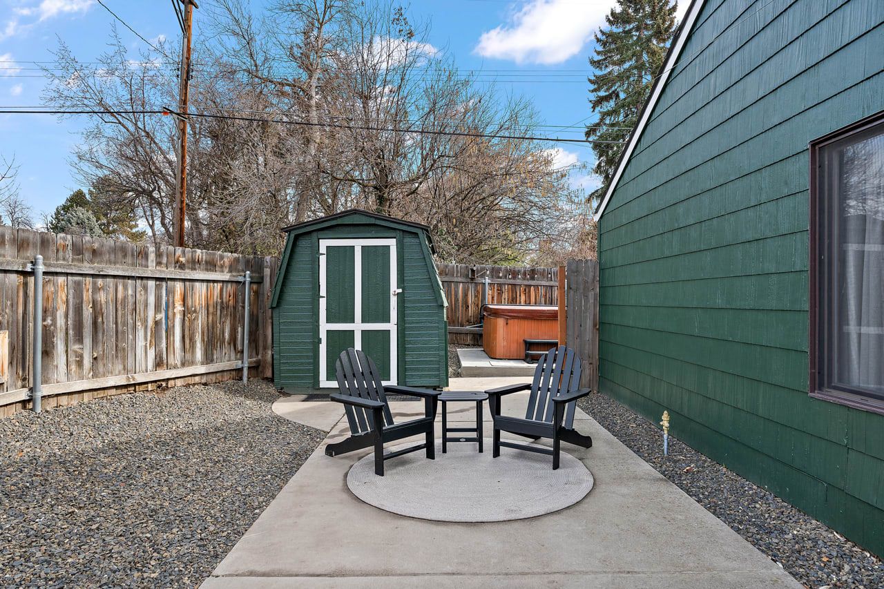 Une terrasse avec deux fauteuils Adirondack et une petite table, une clôture en bois et un abri de jardin avec une porte.
