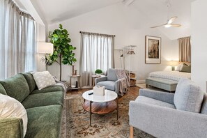 Una sala de estar con un sofá verde, sillones grises, una mesa de centro redonda e un ventilador de techo.