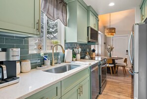 Una cocina moderna con armarios verde azulado, un lavamanos doble, una cafetera y un comedor con mesa y sillas.