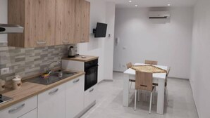 A modern kitchen with wooden cabinets, a built-in oven, and a dining area with a table and chairs. - Lido Apartment Near the sea - air Conditioned (Noto)