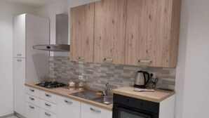 A modern kitchen with white cabinets, a wooden upper section, a tiled backsplash, a gas stove, a sink, a kettle, and a built-in oven. - Lido Apartment Near the sea - air Conditioned (Noto)