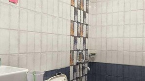 A bathroom with a white toilet, a sink, and a shower. The walls are tiled with a mix of white and dark blue tiles. - VNE Mira Resort (Morjim)