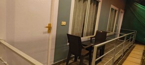 A balcony with a table and chairs, a window with curtains, and a door with a golden handle. - VNE Mira Resort (Morjim)