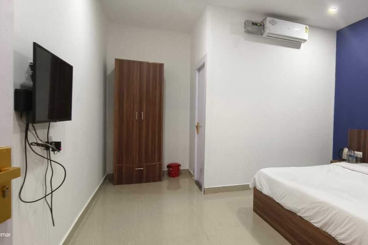 A bedroom with a bed, a wardrobe, a television mounted on the wall, and an air conditioning unit.