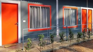 A building with two orange doors and windows with curtains. There are small plants in front of the building. - VNE Mira Resort (Morjim)
