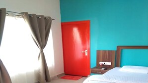 A bedroom with a bed, a red door, and a window with curtains. - VNE Mira Resort (Morjim)