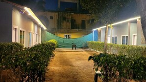 A courtyard with a central pathway, surrounded by buildings with illuminated windows and a green canopy. - VNE Mira Resort (Morjim)