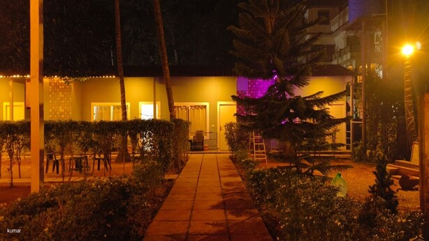 A nighttime view of a hotel courtyard with a paved walkway, palm trees, and a building with illuminated windows. - VNE Mira Resort (Morjim)