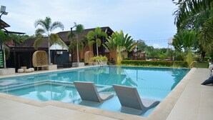 A swimming pool with lounge chairs, palm trees, and a building with a tiled roof.