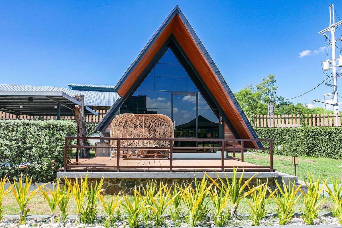 Un bâtiment moderne doté d’un toit triangulaire, d’une façade en verre et d’une terrasse en bois avec un espace salon.