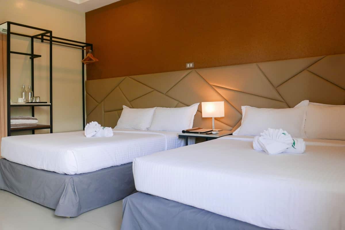 Une chambre d’hôtel avec deux lits, une table de chevet, une lampe, un porte-serviettes et une étagère avec des articles de toilette.