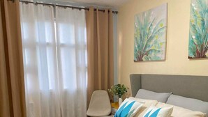 A bedroom with a bed, a chair, a nightstand, and a window with curtains.