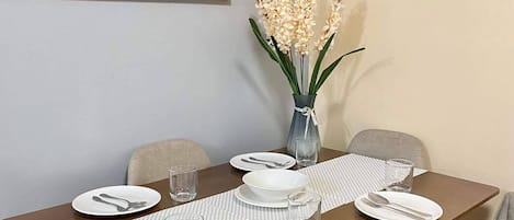 A dining table set with plates, cutlery, and a vase of flowers, with a painting on the wall.