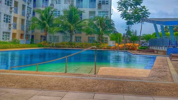A residential building with a swimming pool, palm trees, and a blue sky.